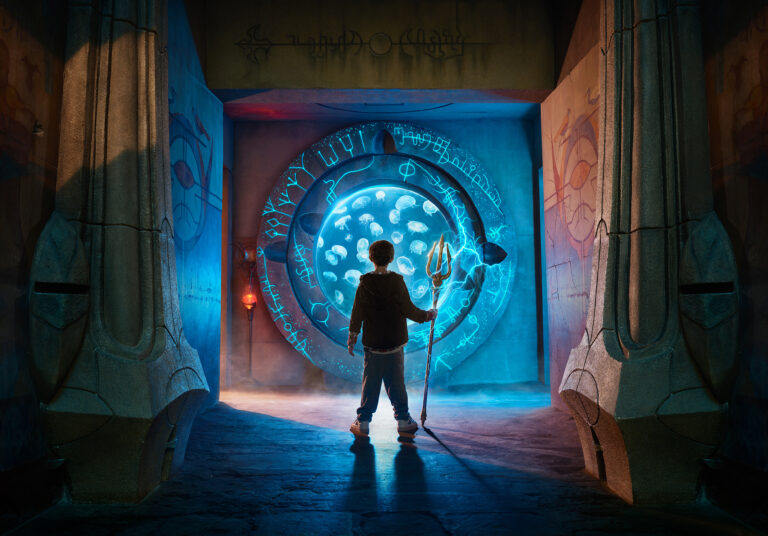 A child stands in front of a jellyfish tank with a trident.